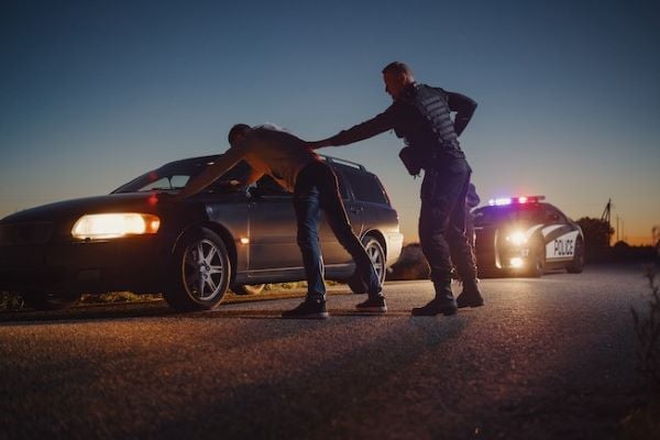 police officer holding suspect with hands on hood of car